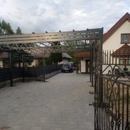 Usługi Ślusarsko Spawalnicze Piotr Wysocki - Metalowa konstrukcja zadaszenia nad podjazdem z widoczną bramą kutą i fragmentem domu w tle.