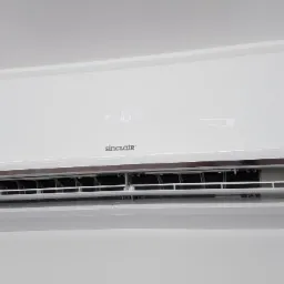 Biała jednostka wewnętrzna klimatyzatora Sinclair zamontowana na jasnej ścianie, widoczny wyświetlacz z temperaturą 16 stopni.