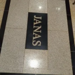 Wykończona podłoga z płytek w odcieniach beżu i czerni z napisem JANAS w centralnej części, widoczne fragmenty obuwia i stóp.