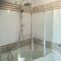 Zamontowana bateria prysznicowa z deszczownicą i szklany parawan nawannowy z trzema składanymi skrzydłami w łazience wykończonej płytkami z poziomymi pasami.