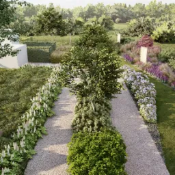 Widok z góry na ścieżkę żwirową w ogrodzie z symetrycznie posadzonymi kwiatami po bokach, drzewami i krzewami, z nowoczesnym białym budynkiem w tle i tablicą informacyjną po lewej stronie.