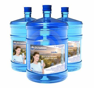 Trzy niebieskie, plastikowe butle z wodą mineralną 'Ostaniec' z etykietą przedstawiającą kobietę i krajobraz, oferowane w Kroczycach.