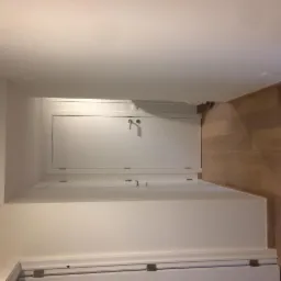 Białe, świeżo pomalowane ściany korytarza z dwiema białymi drzwiami i panelami podłogowymi o wzorze drewna.