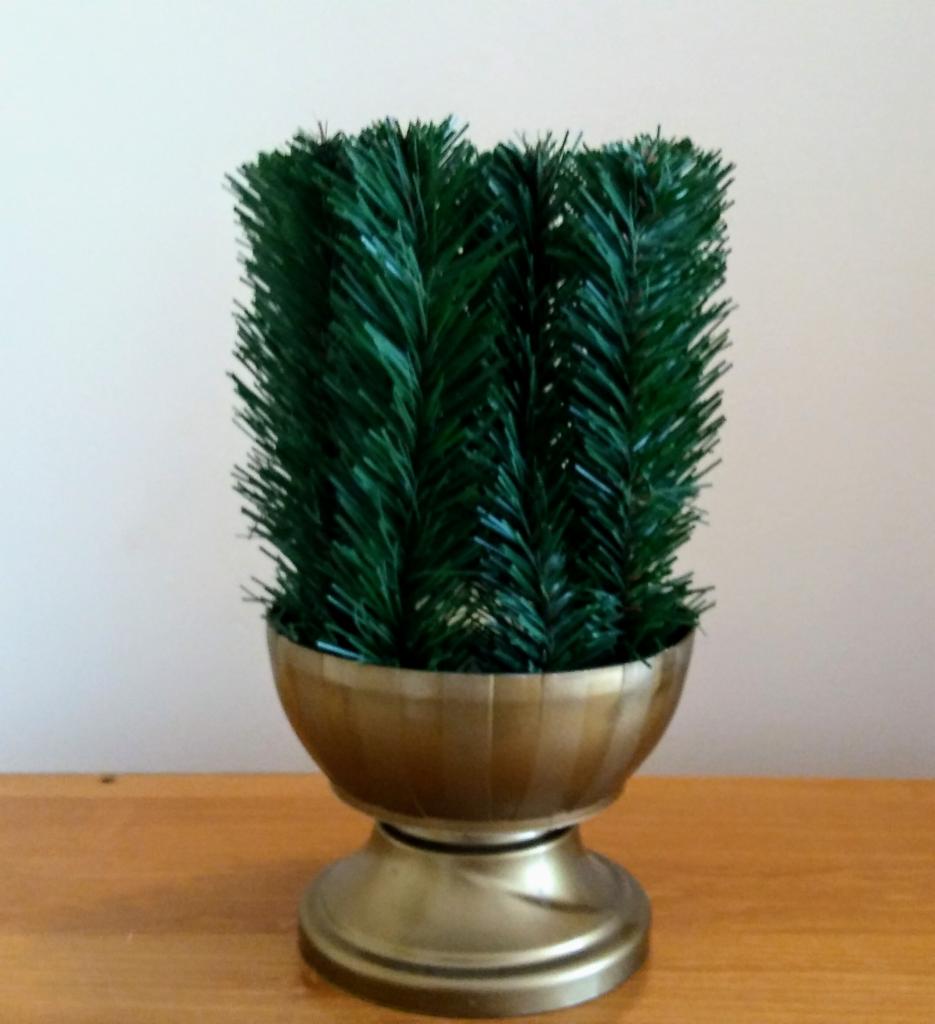 Dekoracyjna, sztuczna choinka w złotej doniczce na drewnianym stole, z bliska.