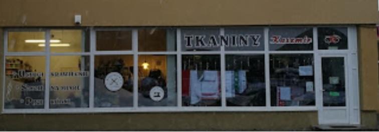 Fasada sklepu z tkaninami i usługami krawieckimi, widoczne napisy 'Tkaniny', 'Usługi krawieckie', 'Szycie na miarę', 'Poprawki', oraz logo z igłą i nitką.