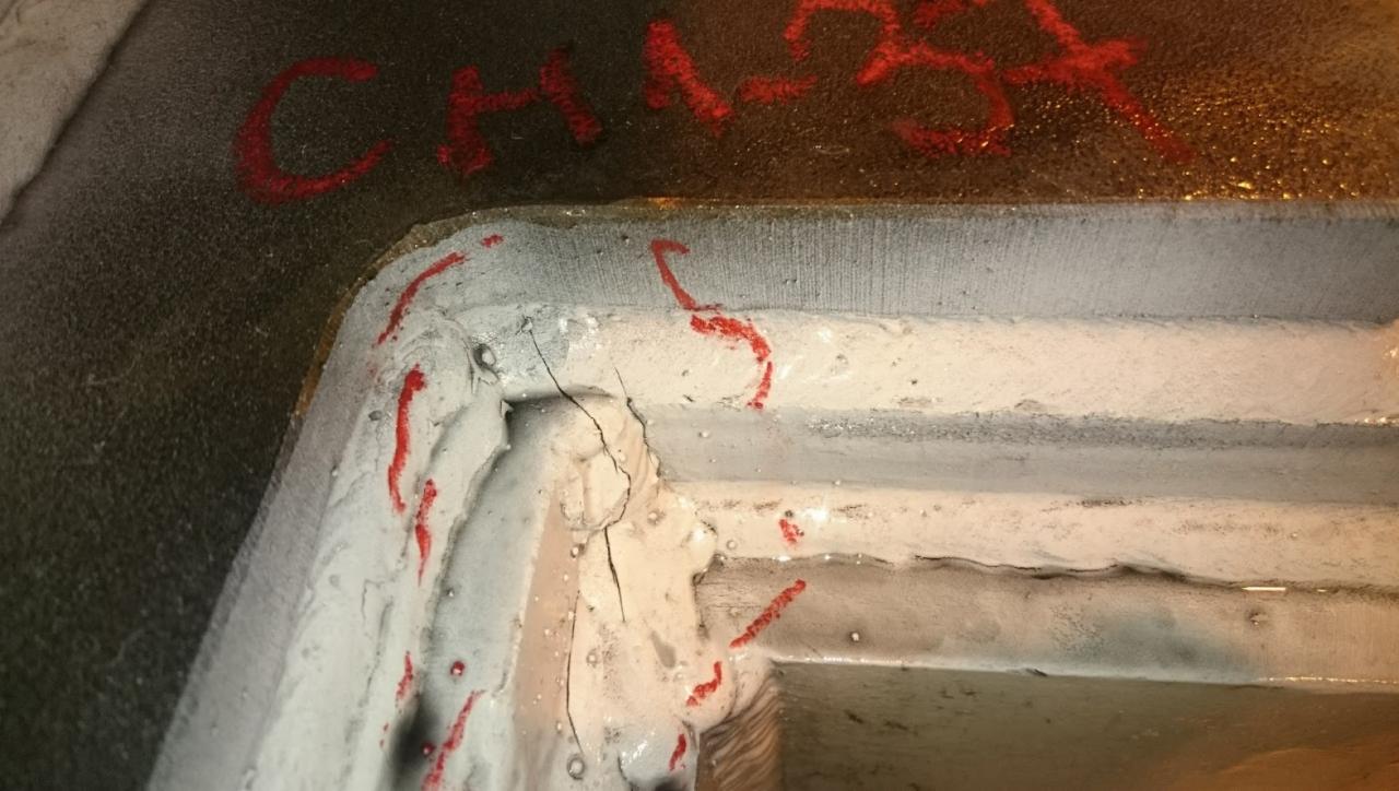 Detal konstrukcji stalowej z widocznym pęknięciem i śladami czerwonej farby, prawdopodobnie oznaczającymi obszar do naprawy.