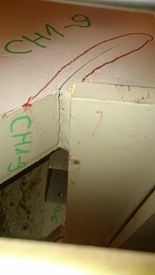 Szczegółowe ujęcie pęknięcia spoiny w konstrukcji stalowej, oznaczenia kontrolne farbą w kolorze zielonym i czerwonym, widoczne ślady korozji.