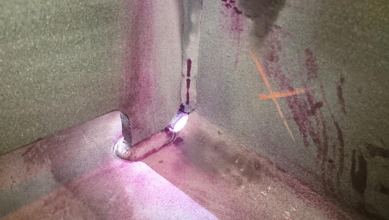 Spoina narożna konstrukcji stalowej z widocznymi śladami kontroli penetracyjnej barwnikowej (DPI), ukazująca potencjalne wady spawalnicze zaznaczone na fioletowo.