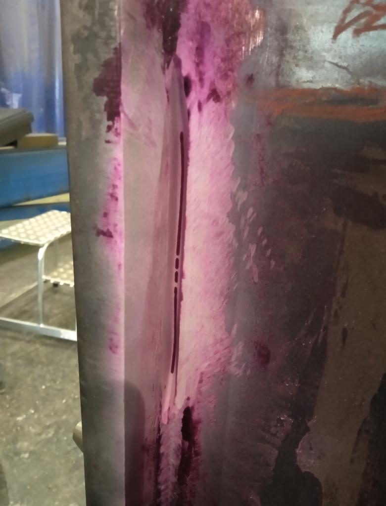 Kontrola jakości spoiny na konstrukcji stalowej metodą penetracyjną, widoczne ślady różowego penetrantu wzdłuż spoiny.