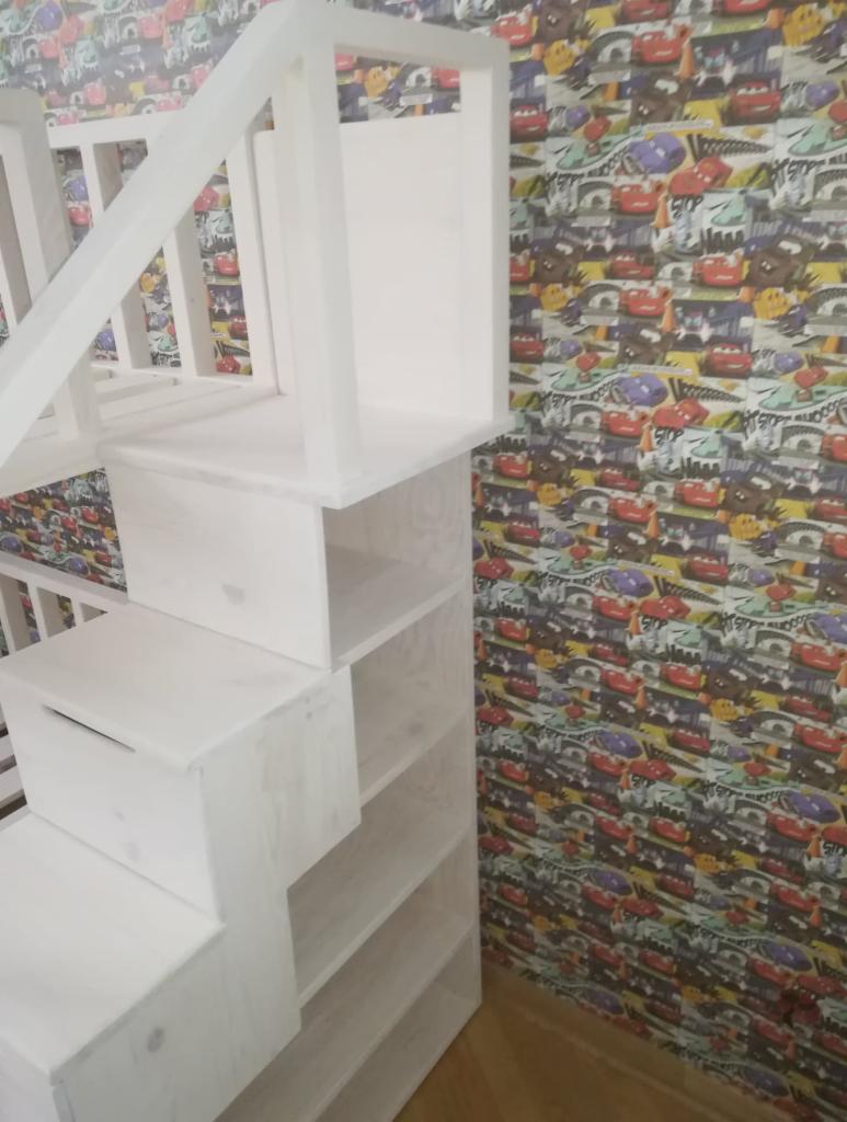 Biała drewniana antresola z drabinką-regałem w pokoju dziecięcym z tapetą w motywy samochodowe.