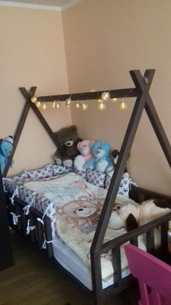 Pokój dziecięcy z łóżkiem w kształcie tipi z drewnianą ramą, ozdobionym lampkami, pluszowymi misiami i pościelą w misie.