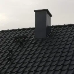 Ciemna dachówka ceramiczna z zamontowanymi stopniami i kominem z blachy w kolorze grafitowym.