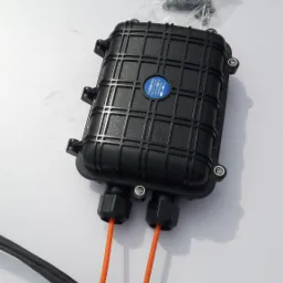 Czarna skrzynka przyłączeniowa z pomarańczowymi kablami światłowodowymi wchodzącymi do niej, umieszczona na białym stole, obok narzędzia i woreczka ze śrubami.