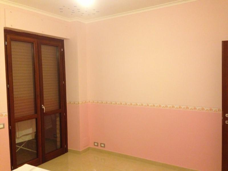 Pokój po malowaniu na różowo, z dekoracyjnym pasem tapety na górze, drewniane okno z żaluzjami i widoczne ślady po gniazdkach elektrycznych.