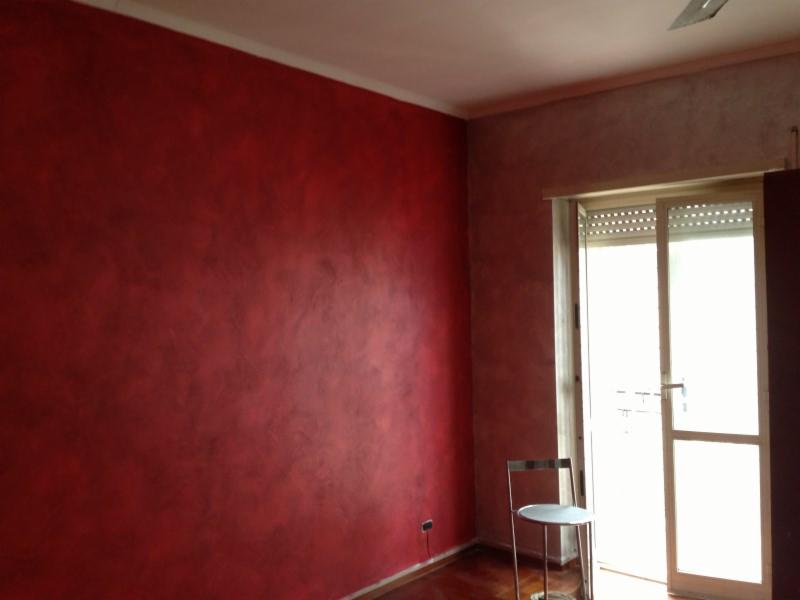 Ściana w odcieniach czerwieni z efektem dekoracyjnym w pokoju w Nowym Targu, widoczny fragment okna balkonowego i krzesło.