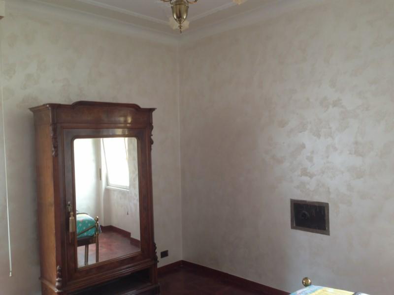 Pokój z dekoracyjną, beżowo-brązową ścianą o nieregularnej fakturze, ciemna drewniana szafa z lustrem oraz kratka wentylacyjna w ścianie.