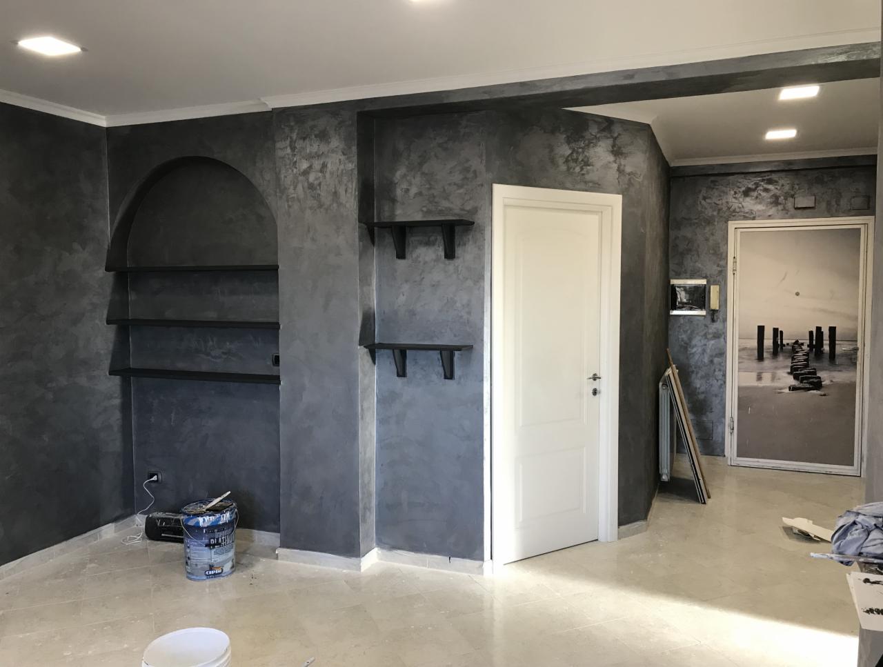 Pokój po wykończeniu ścian dekoracyjną szarą farbą z efektem chmur, z wnęką z półkami i wiszącymi półkami, białe drzwi i fototapeta z motywem molo na plaży w tle.