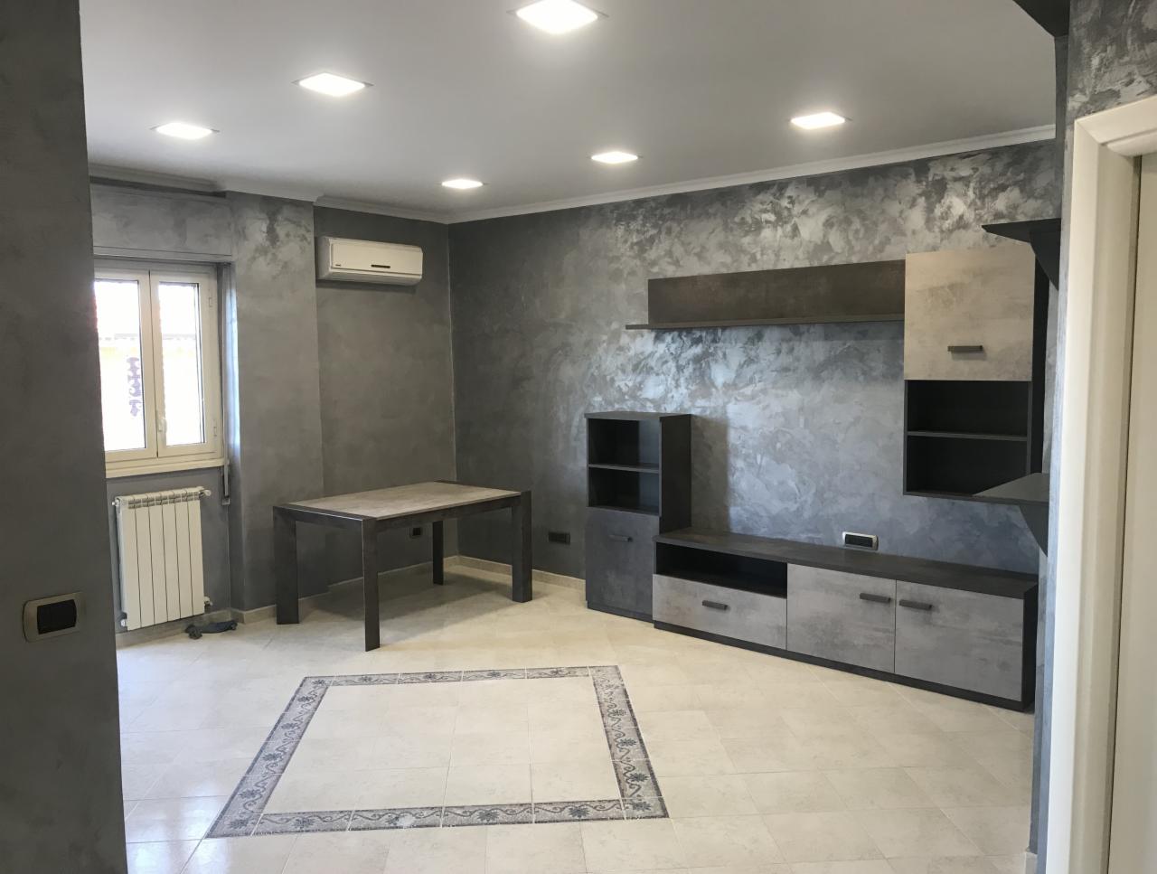 Pokój dzienny po odświeżeniu ścian farbą strukturalną w odcieniach szarości, z nowoczesną zabudową meblową i stołem. Charakterystyczny wzór na ścianie tworzy efekt dekoracyjny.