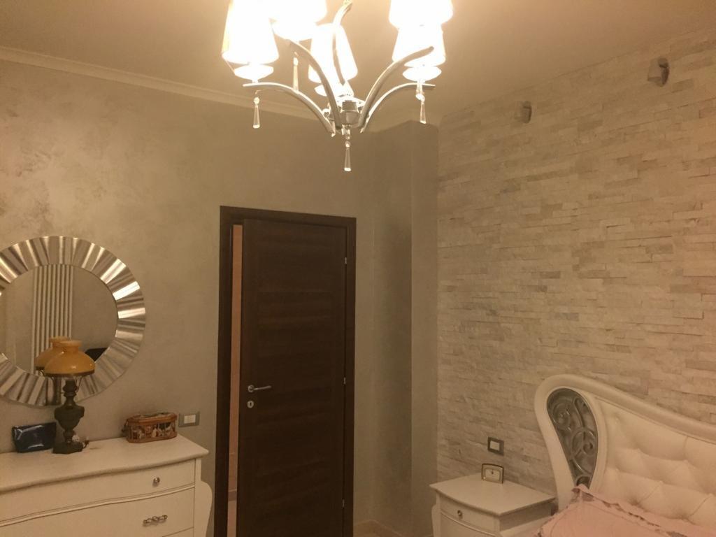 Elegancka sypialnia z dekoracyjną ścianą z kamienia, klasyczną komodą z lustrem w stylu art deco i kryształowym żyrandolem.