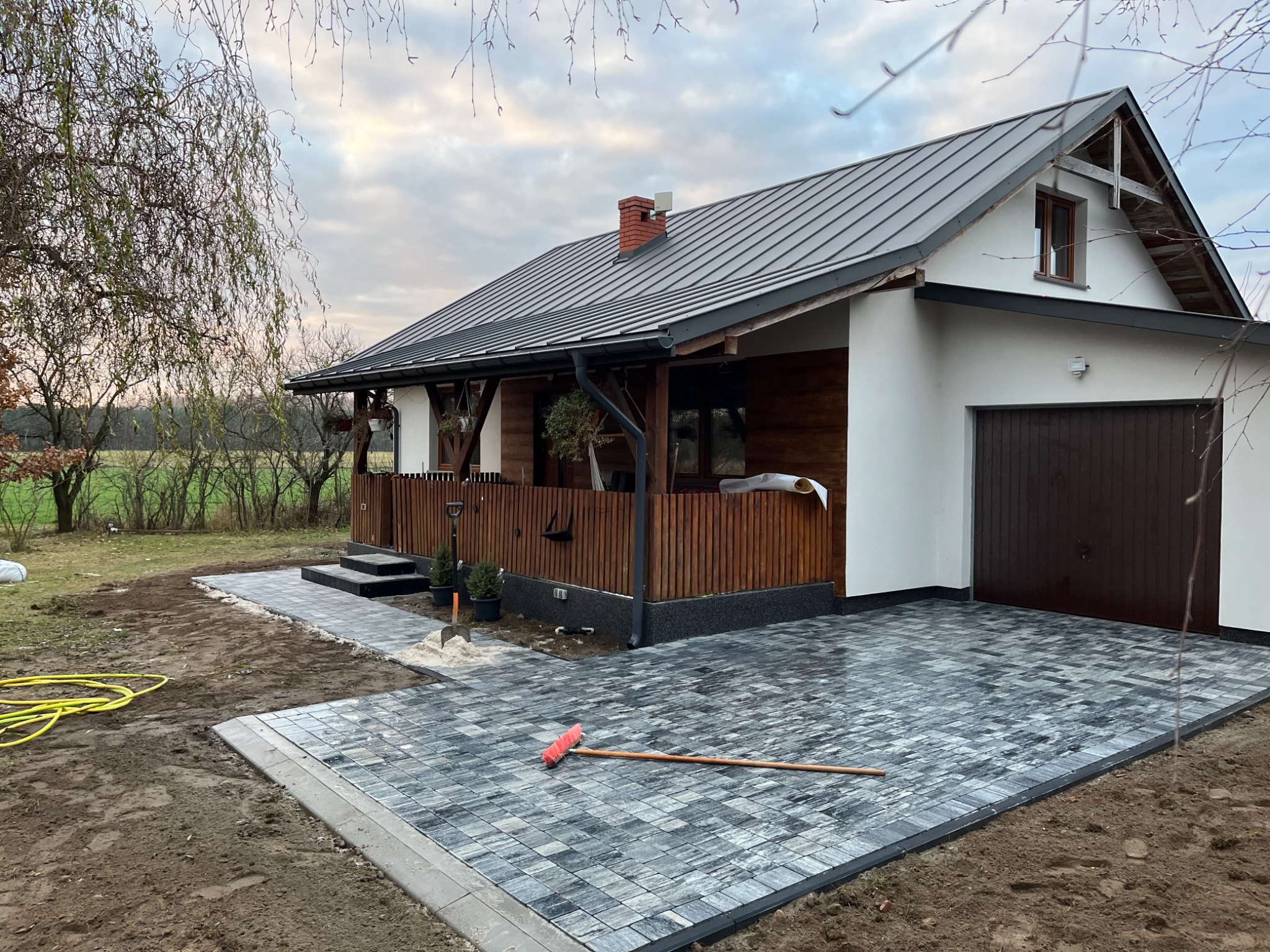 Nowoczesny dom z szarej kostki brukowej na podjeździe i ścieżce, widok z boku, z narzędziem brukarskim na powierzchni.