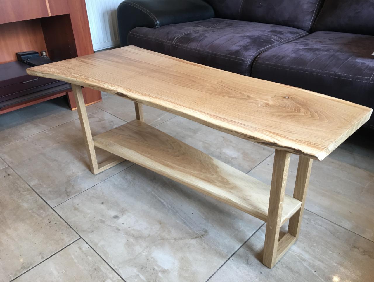 Stolik kawowy z jasnego drewna z półką, surowe krawędzie blatu, na tle sofy i szafki RTV.