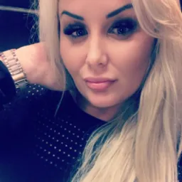 Portret kobiety z blond włosami w czarnej bluzce z metalowym zegarkiem na nadgarstku.