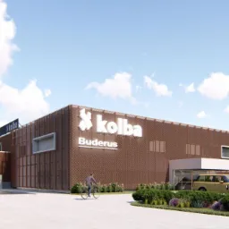 Wizualizacja budynku usługowego z brązową elewacją siatkową, logo Kolba Buderus, rowerzysta na chodniku i zaparkowane samochody.