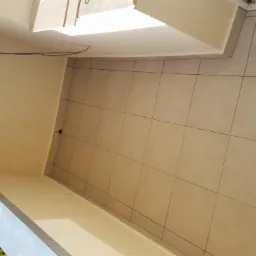 Beżowe, kwadratowe płytki podłogowe ułożone na balkonie, widok z góry, ściany pomalowane na jasny beż, widoczne przewody elektryczne pod sufitem.