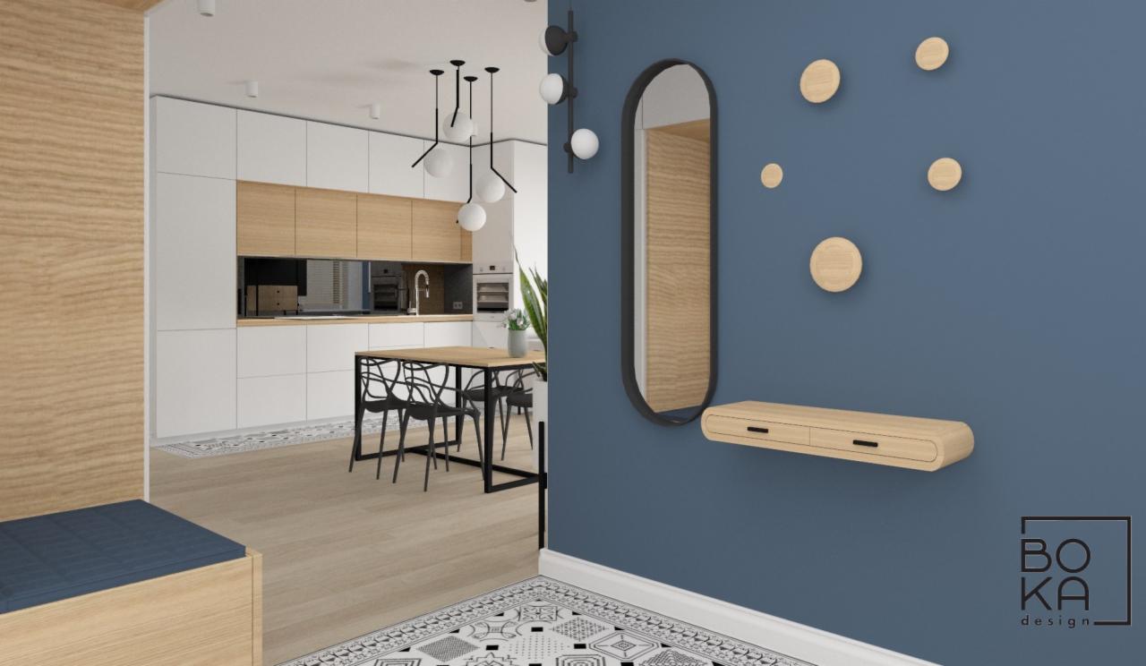 Wizualizacja wnętrza: błękitna ściana z owalnym lustrem w czarnej ramie, drewniana półka z dwiema szufladami, okrągłe drewniane wieszaki, w tle kuchnia z białymi szafkami i drewnianymi blatami...