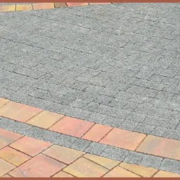 Szara kostka brukowa ułożona w geometryczny wzór z obramowaniem z kolorowej kostki w odcieniach żółci i czerwieni.