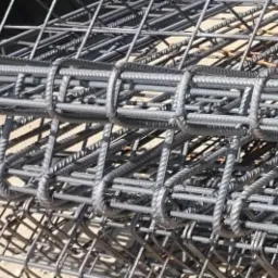 Stalowe zbrojenie w formie gotowych elementów przestrzennych, spięte drutem, przygotowane do zalania betonem, widoczne cienie na podłożu.