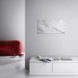 Panel grzewczy imitujący marmur zawieszony na ścianie nad białą szafką w minimalistycznym wnętrzu z czerwonym fotelem.