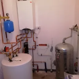 Zainstalowany biały piec gazowy Termet z odprowadzeniem spalin, zbiornik na wodę, niebieskie naczynie przeponowe i rozbudowana instalacja z miedzianych rur w kotłowni.