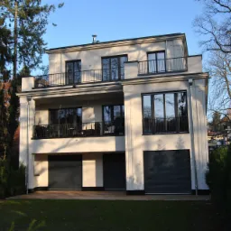 Nowoczesny dom z balkonami zabezpieczonymi metalowymi barierkami, widok z zewnątrz w słoneczny dzień.