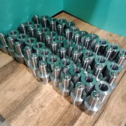 Rząd metalowych, precyzyjnie obrobionych elementów z kulistymi zakończeniami oraz tulei, ułożonych na drewnianej powierzchni w warsztacie.