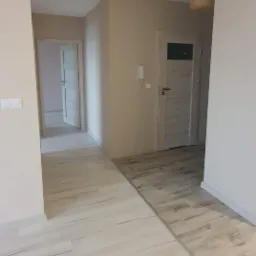 Jasne, wykończone wnętrze mieszkania z panelami podłogowymi imitującymi drewno i dwiema parami drzwi, widok z korytarza.