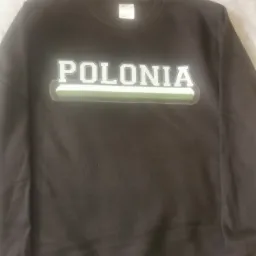 Ciemna bluza dresowa z napisem 'POLONIA' w stylu sportowym, z zielonym akcentem, leżąca na jasnym tle.