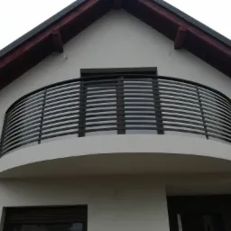 Elewacja budynku z balkonem zabezpieczonym czarną, metalową balustradą o poziomym układzie pręt&oacute;w, widok z dołu.