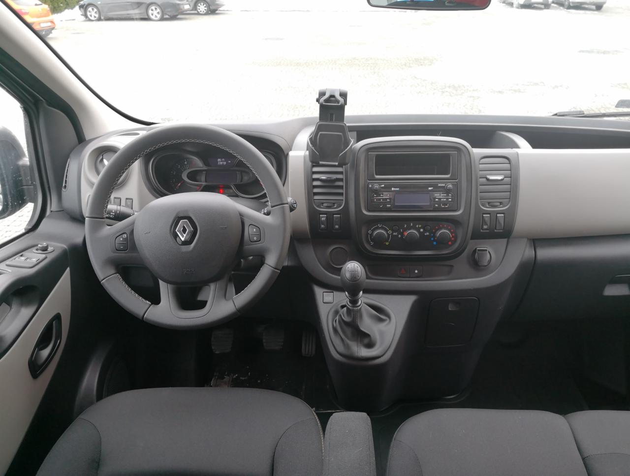 Wnętrze samochodu dostawczego marki Renault z manualną skrzynią biegów, widok na deskę rozdzielczą i kierownicę z szarymi elementami wykończenia.