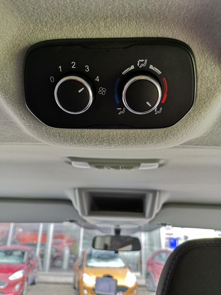Panel sterowania klimatyzacją w samochodzie z widocznymi pokrętłami regulacji temperatury i siły nawiewu, z widokiem na wnętrze salonu samochodowego zza przedniej szyby.