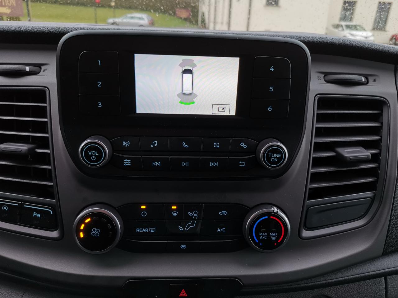 Wnętrze pojazdu z włączonym systemem wspomagania parkowania, wyświetlającym schematyczny widok auta i otoczenia na ekranie centralnym.