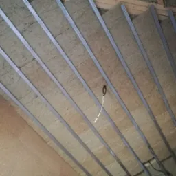 Ocieplenie poddasza wełną mineralną, widoczne metalowe profile montażowe, częściowo zakryte płyty gipsowe.