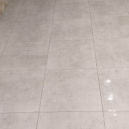 Łukasz Woznica - Wykończone wnętrze z jasnoszarą, kwadratową podłogą z płytek i dekoracyjną ścianą z imitacji kamienia w odcieniach beżu.