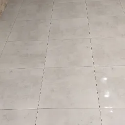 Wykończone wnętrze z jasnoszarą, kwadratową podłogą z płytek i dekoracyjną ścianą z imitacji kamienia w odcieniach beżu.