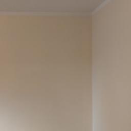 Łukasz Woznica - Pusty pokój po malowaniu ścian na jasny, kremowy kolor, z widoczną drewnianą podłogą i listwami przypodłogowymi. Na ścianie widoczne ślady po otworach.