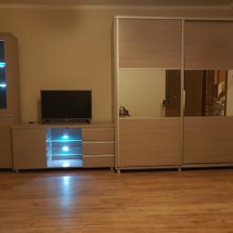 Łukasz Woznica - Jasne meble w salonie: szafa przesuwna z lustrami, szafka RTV z podświetleniem LED i wysoka witryna, parkiet na podłodze.