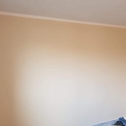 Łukasz Woznica - Jasna, beżowa ściana po malowaniu z widoczną listwą przypodłogową przy suficie i zabezpieczeniem podłogi folią malarską w dolnym rogu.