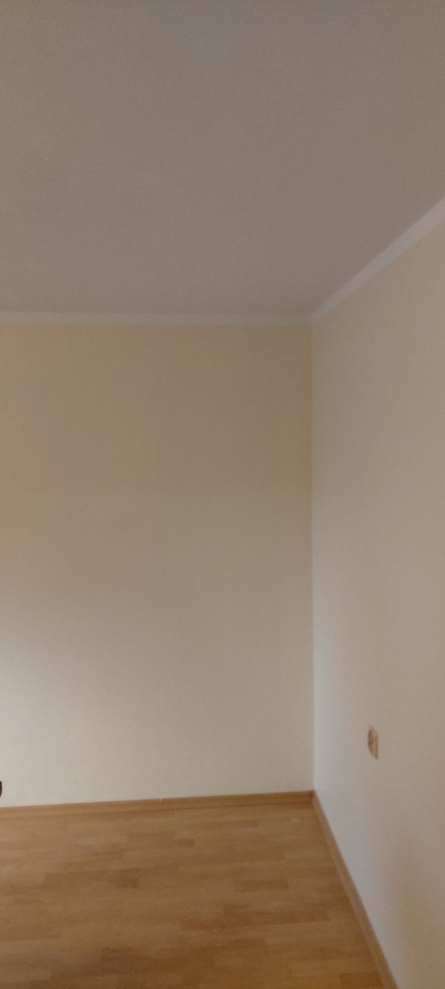 Pusty pokój po malowaniu ścian na jasny, kremowy kolor, z widoczną drewnianą podłogą i listwami przypodłogowymi. Na ścianie widoczne ślady po otworach.