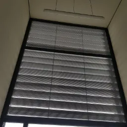 Wysokie okno z zamontowanymi żaluzjami poziomymi, widok z dołu, w tle lampa sufitowa.