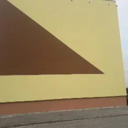 Wykonana elewacja budynku w Blizanowie z geometrycznym wzorem, łącząca odcienie brązu i beżu, widok od dołu ukazujący fragment chodnika i trawnika.